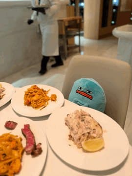 Blob sitting on a restaurant chair behind plates of pasta and steak