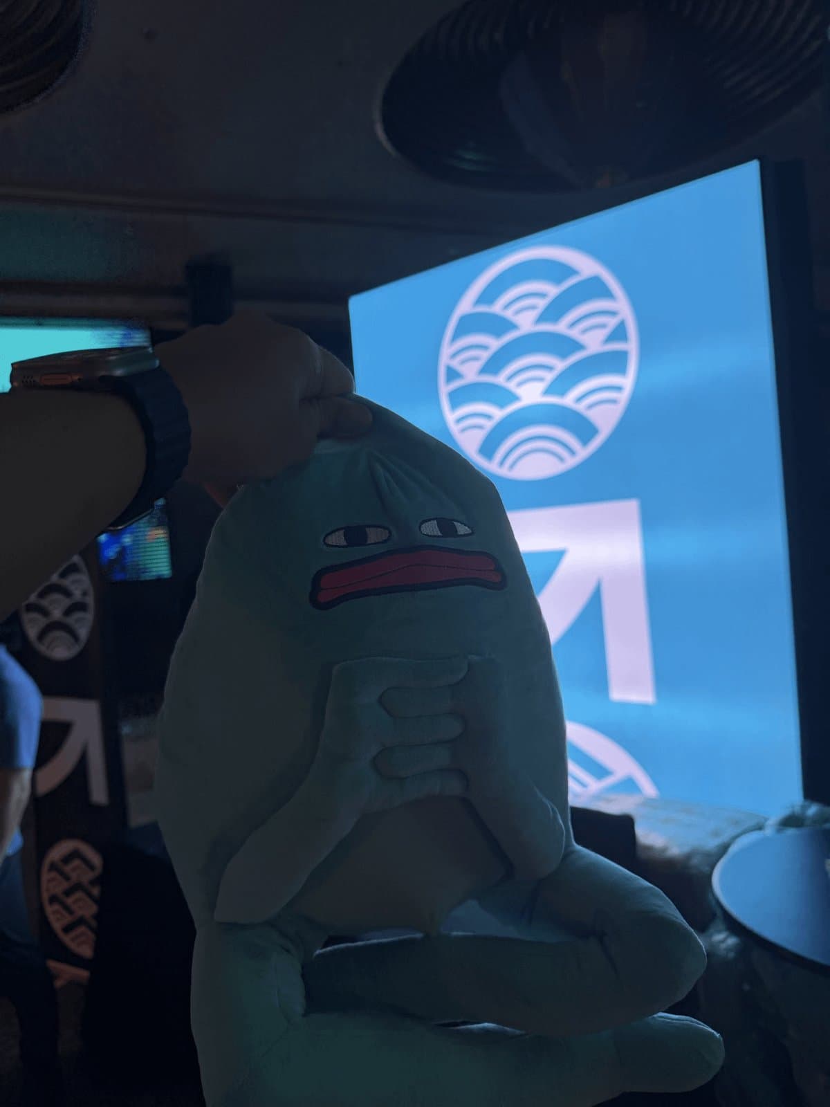 A hand holding Blob up by the top of its head in front of a glowing blue event screen
